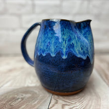 Load image into Gallery viewer, no two are exactly alike. wheel thrown and handcrafted stoneware pottery pitcher in Blue world glaze. The pitcher is a dark cobalt blue on the bottom layer with a unique layering of turquoise and bright blue dripping down the top half of the pitcher.
