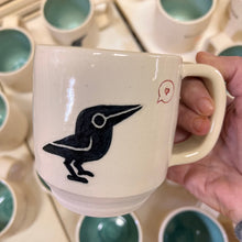 Load image into Gallery viewer, artisan made, wheel thrown pottery mug. porcelaina clay, with a cute crow or raven image that is painted on and carved into it. the crow speaks of love at it is speaking a heart in a speech bubble.