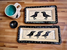 Load image into Gallery viewer, crow or raven carved pottery platter shown with crow mug and tiny bowls.. crows are sgraffito carved into the center with footprints around the edge. stoneware, black on white clay.