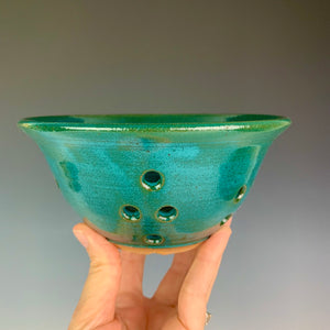 Berry colander in teal glaze on red clay. shown being held by the artist for scale. holds a pint to a pint and a half