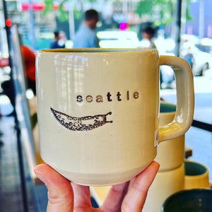  Wheel thrown pottery mug with "seattle" and an image of a slug inset on the outside. white outside, turquoise green glaze interior