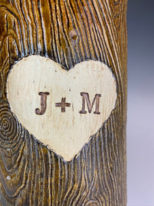 closeup of wood grain textured vase, appears like a tree thrunk with a heart caved into it and initials carved into the heart.
