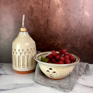 Olive oil cruet, shown with a pint sized berry colander.. Wheel thrown and carved. cork stopper  for smooth pouring. Thrown in a red stoneware clay and carved by hand. the white glaze accentuates the carved pattern where the red clay shows through.