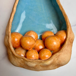 closeup, detail shot of See Pod inspired wall sculpture, stoneware husk like nest of seeds or eggs in light orange with a blue interior
