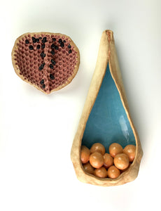 closeup, detail shot of See Pod inspired wall sculpture, stoneware husk like nest of seeds or eggs in light orange with a blue interior. shown here hanging with another seedpod sculpture