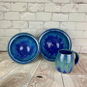 wheelthrown blue world bowls shown with a matching mug. the bowl is glazed in cobalt blue with turquoise green glaze melting down into the blue from the rim of the bowls. 