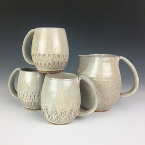 pitcher in speckled white shown with various carved mugs.