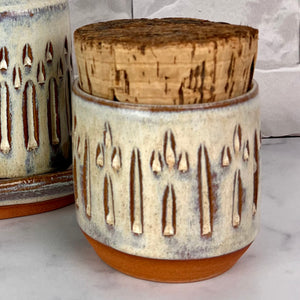 Canister for beautiful display and storage. this canister is made from red stoneware clay, carved with a pattern and glazed in a speckled white glaze. the canister has a natural, rough cork lid. approximately 3.5 inches wide and 3.5 inches tall