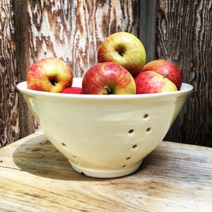 large pottery colander in pure white glaze, shown full of apples, rustic wood background