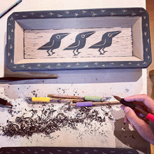 Load image into Gallery viewer, work in process: an image of the artist carving crow patterns into a &#39;leather hard&quot; clay paltter using diamondcore carving tools. each platter is handcrafted and hand carved in the traditional sgraffito process. 