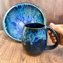 Load image into Gallery viewer, Blue World Mug! a dark blue glaze base on a red stoneware mug. the top of the mug is glazed in layered blue glazes that undulate and drip. Each one is unique. Holds 14-16 oz and has a full handle grip with groovy thumb groove. Shown here with Blue World servig bowl.