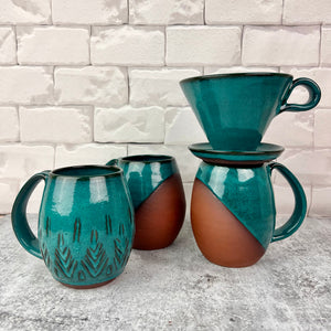 Set of ceramic mugs with a coffee pour over on one. one carved mug, two angle dipped mugs in teal.