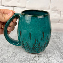 Load image into Gallery viewer, Beautiful, vibrant teal glaze on a hand carved northwest mug. the carvings allow the glaze to show through a bit at the edges, bringing variation to the glaze.