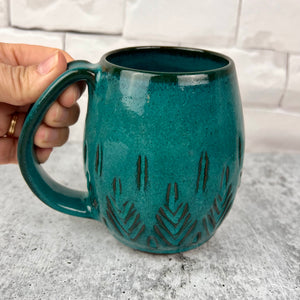 Beautiful, vibrant teal glaze on a hand carved northwest mug. the carvings allow the glaze to show through a bit at the edges, bringing variation to the glaze.