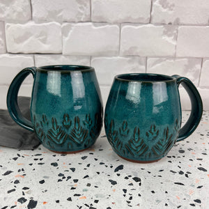 Beautiful, vibrant teal glaze on hand carved northwest mugs. the carvings allow the glaze to show through a bit at the edges, bringing variation to the glaze.