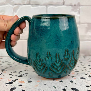 Beautiful, vibrant teal glaze on a hand carved northwest mug. the carvings allow the glaze to show through a bit at the edges, bringing variation to the glaze.