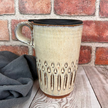 Load image into Gallery viewer, a wheel thrown pottery travel mug. each one is hand carved, this version is the &quot;vertical pattern&quot; carving. finger loop handle, shown here with fitted travel lid, fits into most cup holders.