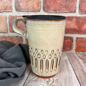 a wheel thrown pottery travel mug. each one is hand carved, this version is the "vertical pattern" carving. finger loop handle, shown here with fitted travel lid, fits into most cup holders.