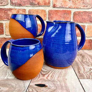 Pottery pitcher shown in blue with matching salt cellar, and oil cruet. pitcher can be used as a pitcher, utensil holder, or vase.Stoneware pottery pitcher in Cobalt Blue on Red Stoneware with pulled handle. handcrafted and wheel thrown at Fern Street Pottery