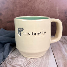 Load image into Gallery viewer, Wheel thrown pottery mug, made from porcelaina ( a porcelain stoneware) and hand stamped with the town of indianola and a jumping salmon. glazed turquoise on the inside of the mug.