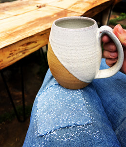 The artist holding an angle dipped mug in speckled white. wheel thrown, stoneware mug with a pulled handle