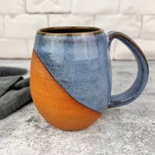 Load image into Gallery viewer, Wheelthrown mug, handcrafted with pulled handle. Angle dipped glaze pattern which leaves some of the natural red clay exposed for a tactile experience. This mug is shown in &quot;icy blue&quot; which is a beautiful glossy and richly mottled glaze.