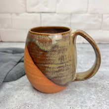 Load image into Gallery viewer, Wheelthrown mug, handcrafted with pulled handle. Angle dipped glaze pattern which leaves some of the natural red clay exposed for a tactile experience. This mug is shown in &quot;caramel&quot; which is a beautiful glaze that shows the beautiful layers and transparency.