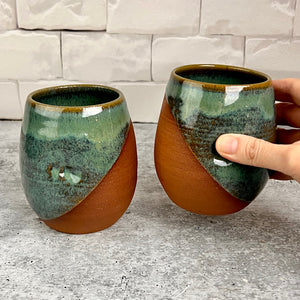 set of two pottery tumblers. Red stoneware clay, glazed in moss green glaze which subtly shows the clay through the glaze. tumblers have finger divots and are dishwasher safe. great at wine glasses cocktail glasses, water glasses.