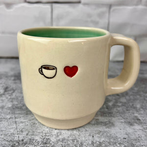 Image of a coffee mug and a red heart, stamped into the mug. artist thrown in White clay, turquoise glaze on the inside. this mug was wheel thrown and hand stamped and colored at fern street pottery.