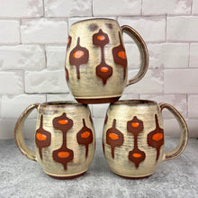 Load image into Gallery viewer, Three ceramic mugs with abstract patterns stacked on a light gray surface against a white brick wall. Handcrafted, wheel thrown mug by Meredith Chernick at Fern Street Pottery. Hand painted resist and glaze pattern in light dijon yellow, deep red stoneware clay, and bright orange dots. 