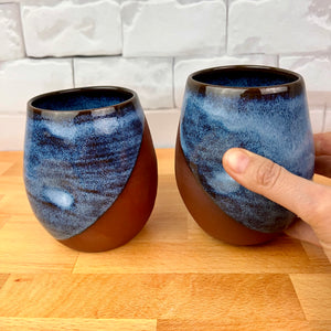 set of two pottery tumblers. Red stoneware clay, glazed in Icy Blue glaze which subtly shows the clay through the glaze. tumblers have finger divots and are dishwasher safe. great at wine glasses cocktail glasses, water glasses.