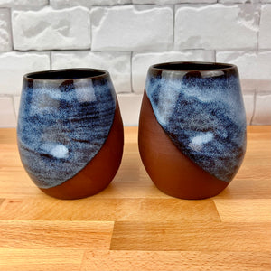 set of two pottery tumblers. Red stoneware clay, glazed in Icy Blue glaze which subtly shows the clay through the glaze. tumblers have finger divots and are dishwasher safe. great at wine glasses cocktail glasses, water glasses.