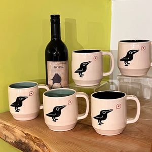 a murder of crow mugs! shown in both turquoise interior and black interior.artisan made, wheel thrown pottery mug. porcelaina clay, with a cute crow or raven image that is painted on and carved into it. the crow speaks of love at it is speaking a heart in a speech bubble. 
