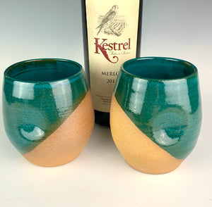 Stemless wine glasses. set of two wheel thrown pottery with finger divots for grip. Teal green glaze over red stoneware clay, glazed at an angle to reveal the clay. shown with wine