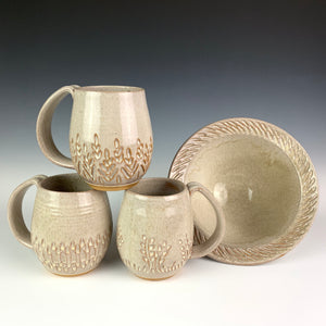 Carved mugs pictured with a carved rim serving bowl. the pots are thrown on the potters wheel in a red brown clay, then glazed in white. bowl is approximately 7" in diameter 