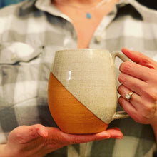Load image into Gallery viewer, Fern Street Pottery artist, Meredith Chernick holds an Angle-dipped mug. The mug is thrown from red clay and is dipped in speckled white glaze, showing the texture of the clay through. The handle is a full grip, 4 finger handle (for most).