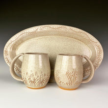 Load image into Gallery viewer, wheel thrown and hand carved mugs. the mug is thrownin red stoneware which shows throught the white glaze at the edges of the mug. the mugs have delicate patterns carved into them. shown here with a matching carved platter