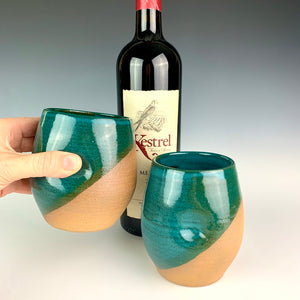 Stemless wine glasses. wheel thrown pottery with finger divots for grip.  Teal green glaze over red stoneware clay, glazed at an angle to reveal the clay. shown with wine.