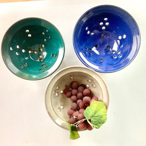 berry colanders, shown in teal, speckled white and cobalt blue. shown for rinsing berries or grapes
