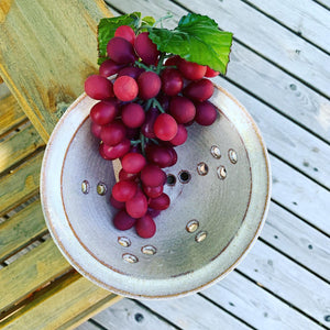 berry colander in speckeld white glaze, shown with grapes. photo taken on an adirondack chair on the deck