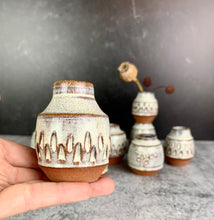 Load image into Gallery viewer, a collection of small bud vases , each one is hand carved with facets, with dried flowers in one of them. the vases are about 1.5-2 inches tall, wheelthrown in red stoneware, 