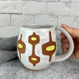 wheelthrown Pottery mug, hand glazed with MidMod pattern in white, and yellow, with the deep red clay showing in the resist pattern