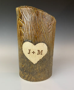 wood grain textured vase, appears like a tree thrunk with a heart caved into it and initials carved into the heart.