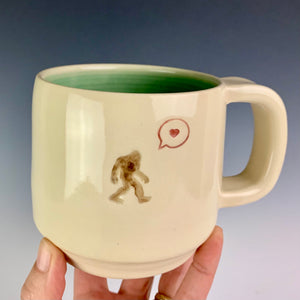 Sasquatch with a heart bubble on an artist made, wheel thrown pottery mug. Beautiful porcelaina creamy white clay with a turquoise glaze on the inside.