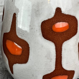 detail shot of the glaze pattern on a midmod mug. wheelthrown Pottery mug, hand glazed with MidMod pattern in white, and orange, with the deep red clay showing in the resist pattern