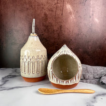 Load image into Gallery viewer, Olive oil cruet, shown with salt cellar. Wheel thrown and carved. cork stopper  for smooth pouring. Thrown in a red stoneware clay and carved by hand. the white glaze accentuates the carved pattern where the red clay shows through.