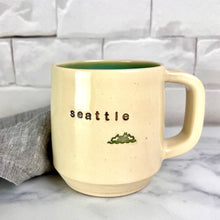 Load image into Gallery viewer,  Wheel thrown pottery city mug with &quot;seattle&quot; and an image of a ferry inset on the outside. white outside, turquoise green glaze interior