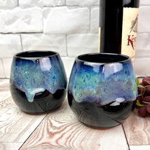 Load image into Gallery viewer, Stemless wine glasses. set of two wheel thrown pottery with finger divots for grip. Black glaze on the tumbler with bright blues and turquoise colors mixed similar to the Aurora Borealis as a glaze over stoneware clay
