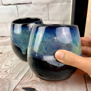 Stemless wine glasses. set of two wheel thrown pottery with finger divots for grip. Black glaze on the tumbler with bright blues and turquoise colors mixed similar to the Aurora Borealis as a glaze over stoneware clay