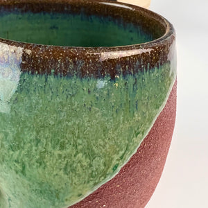 detail shot of glaze on Deep green wine glass. showing the deep red clay and the detail of the glaze. note the blues and browns on the rim